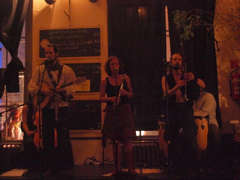 Ein Band, bestehend aus 2 Männern (außen) und einer Frau (Mitte) spielen ihre Instrumente und singen.
