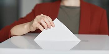 Frau wirft Wahlzettel in die Wahlurne.