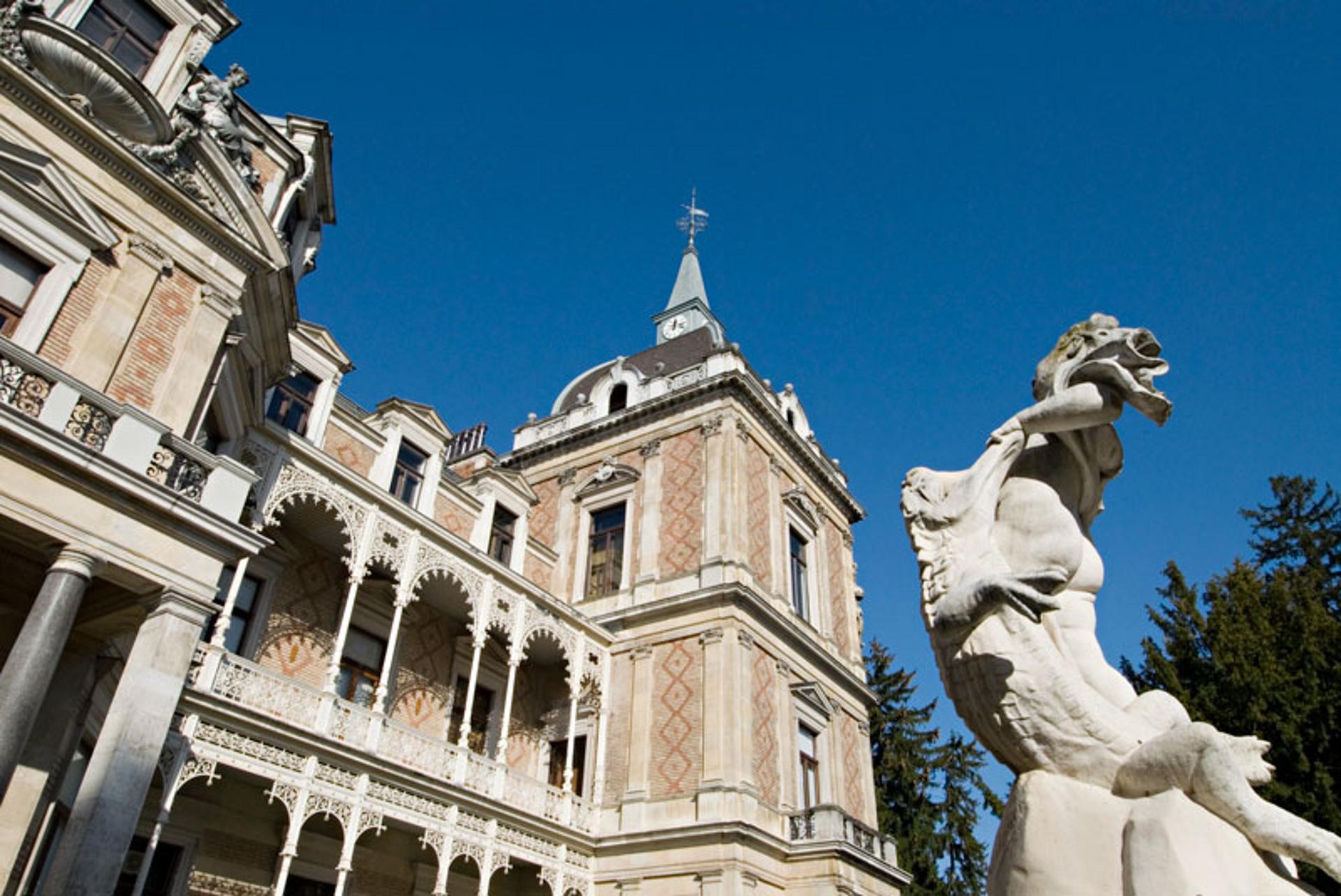 Seitenturm einer prunkvollen Villa mit einer weißen Statue im Vordergrund.