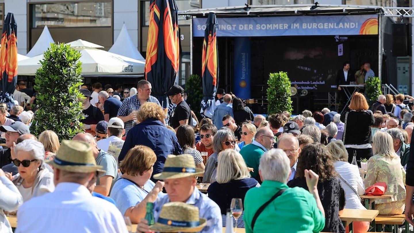 Festbänke und Schirme, viele Menschen, eine Bühne Am Hof in Wien