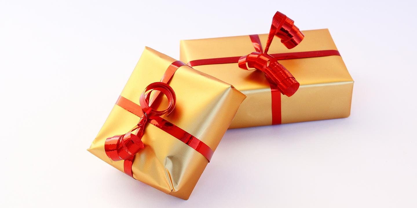 Zwei golden eingepackte Geschenke mit roten Schleifen