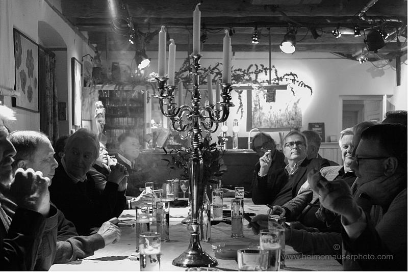 Männer eines Zigarrenclubs rund um einen Tisch mit Kerzenleuchter in der Mitte