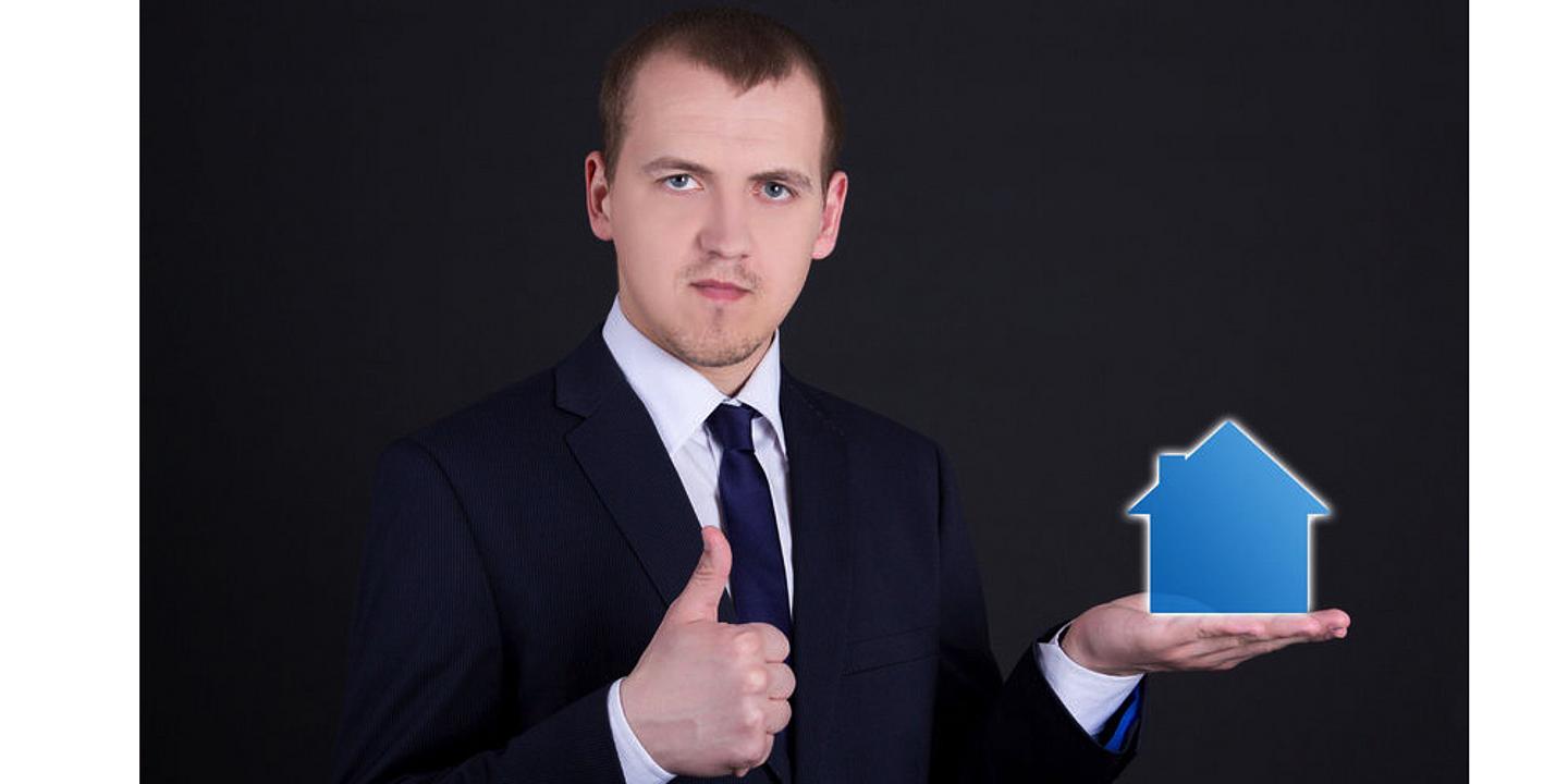 Mann hält Haus in einer Hand und zeigt thumbs up