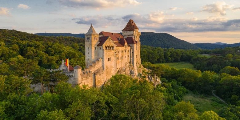 Steinerne Burganlage mit Türmen und Zinnen, teilweise bewaldeter Hügelhang im Vordergrund; Burg Liechtenstein bei sonnigem Wetter.