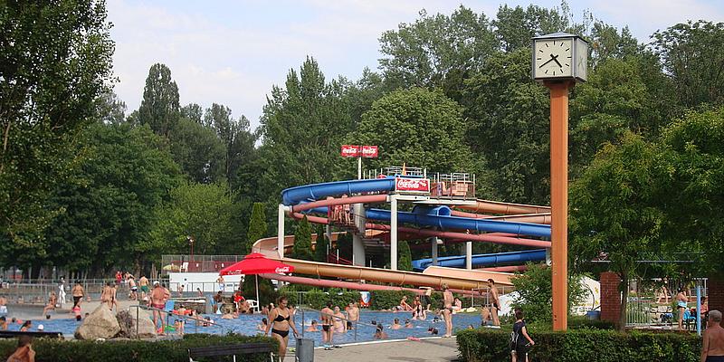 Rutschen im Stadionbad Ein Becken mit vielen Menschen, dahinter eine lange Rutsche.