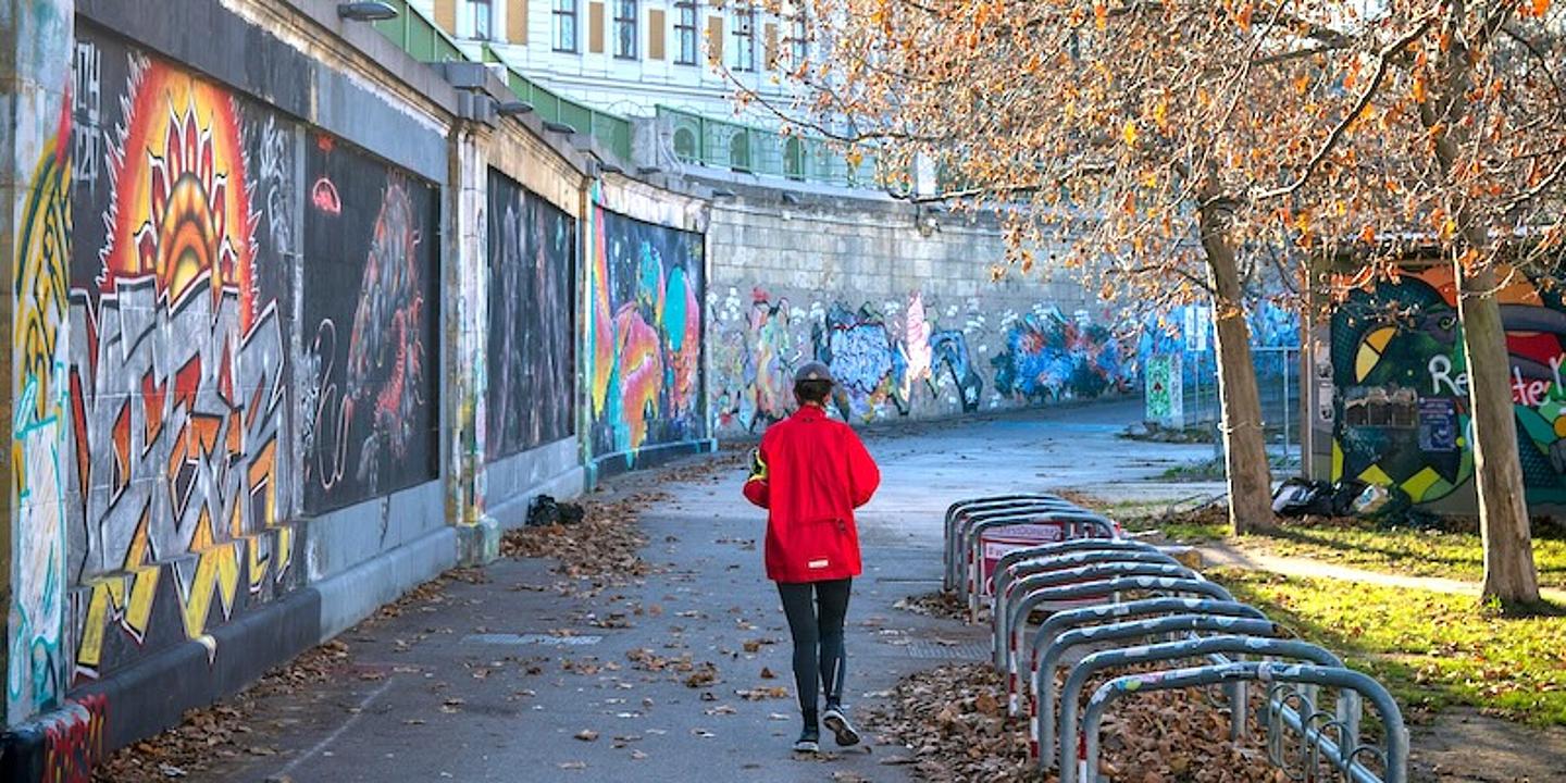 joggerin von hinter am wiener donaukanal mit graffitti Wand links