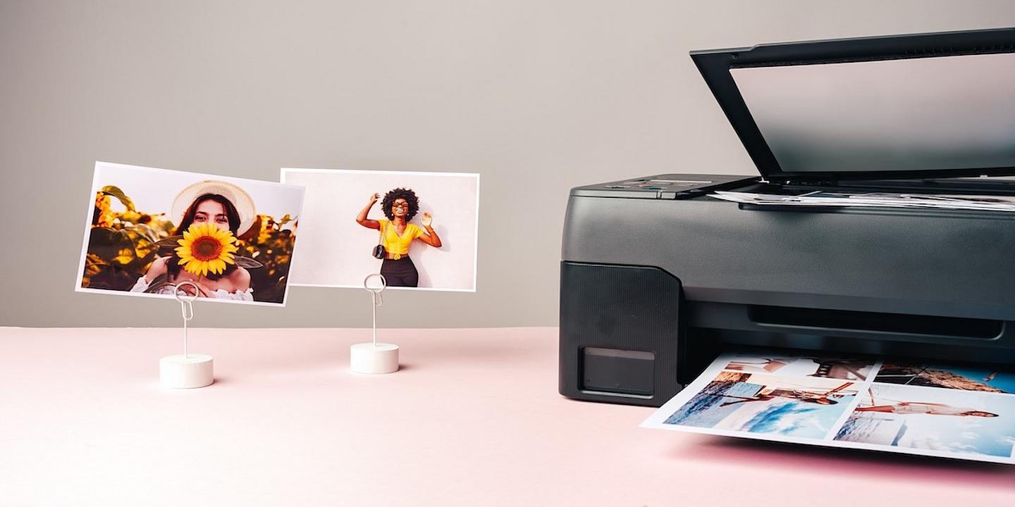 drucker mit fertigem Ausdruck im Fach, daneben 2 Fotos am Ständer