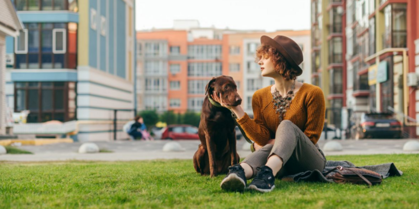 Frau sitzt mit Hund auf einer Wiese mitten in der Stadt