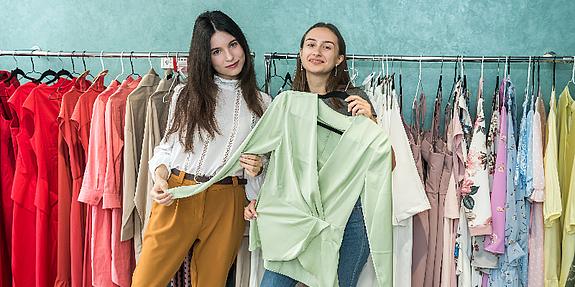 Zwei Mädchen die glücklich einen Pullover austauschen, Kleidertausch in Wien