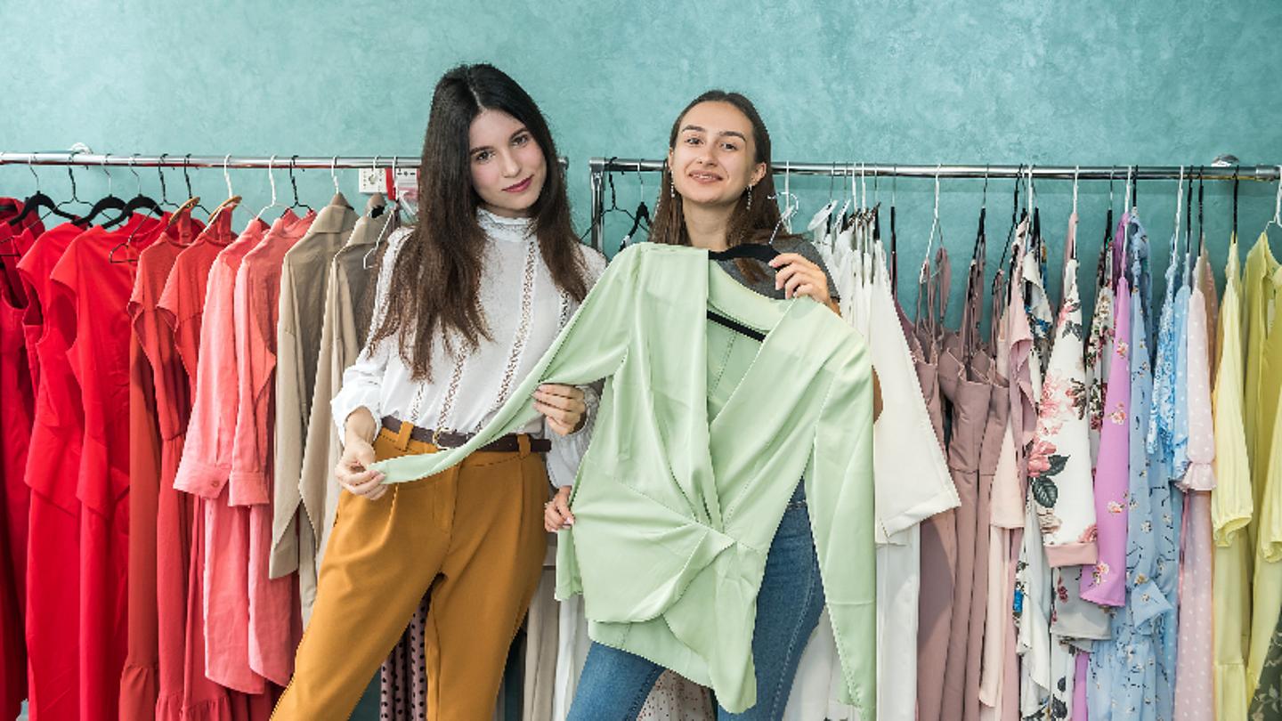 Zwei Mädchen die glücklich einen Pullover austauschen, Kleidertausch in Wien
