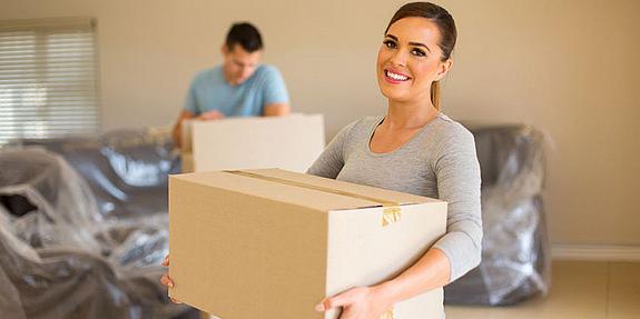 Eine Frau trägt Schachtel im Hintergrund verpackte Couch