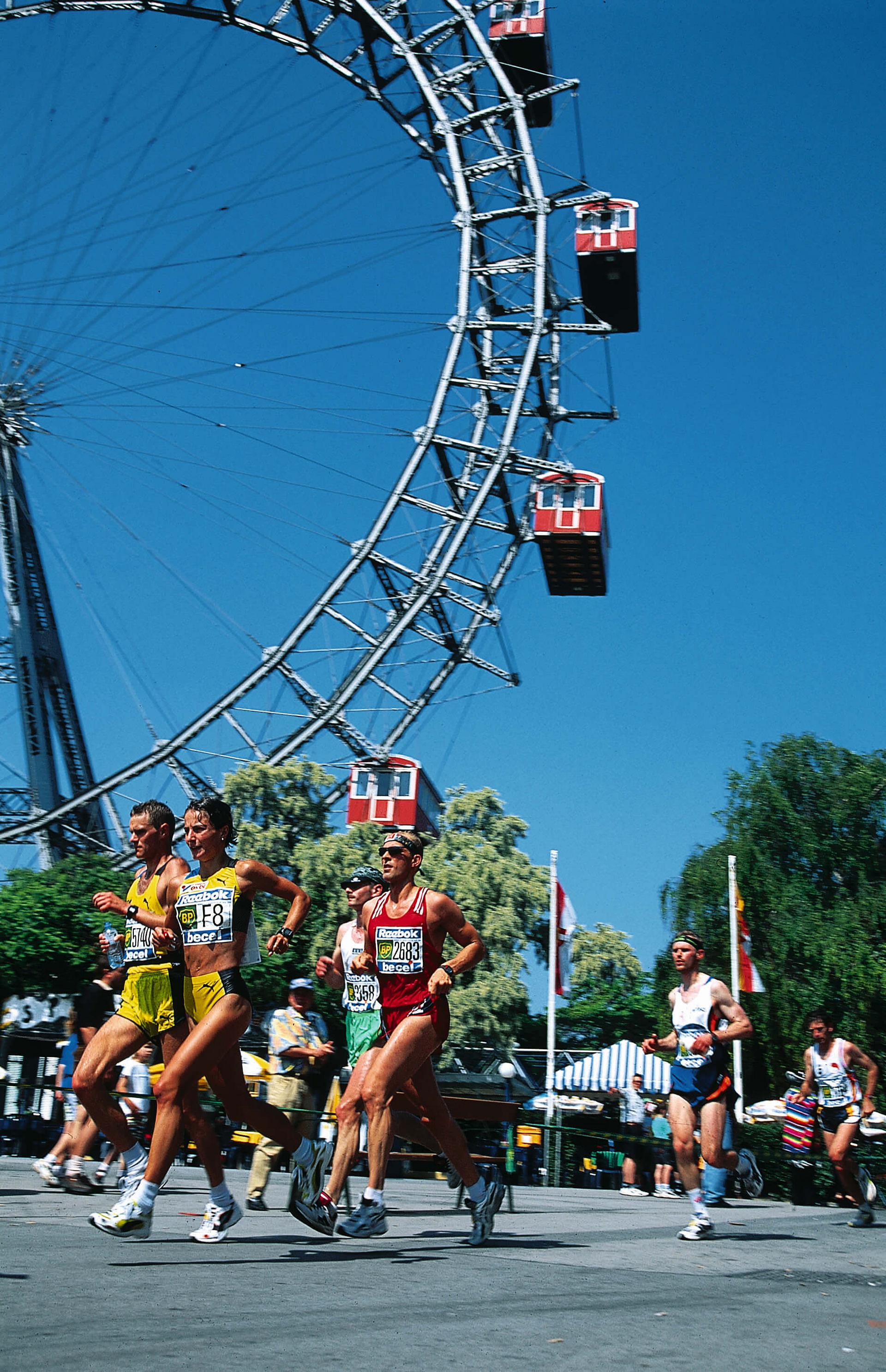 Die Sportlerinnen und Sportler laufen am Riesenrad vorbei.