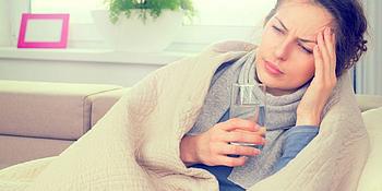 Frau liegt auf Couch mit Glas Wasser in der Hand und ist krank wegen Biowetter