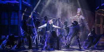 Musicalszene mit Ebenezer Scrooge und drei Weihnachtsgeistern vor winterlicher Kulisse- festlich beleuchtete Bühne mit weihnachtlicher Stimmung.