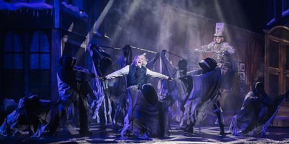 Musicalszene mit Ebenezer Scrooge und drei Weihnachtsgeistern vor winterlicher Kulisse- festlich beleuchtete Bühne mit weihnachtlicher Stimmung.