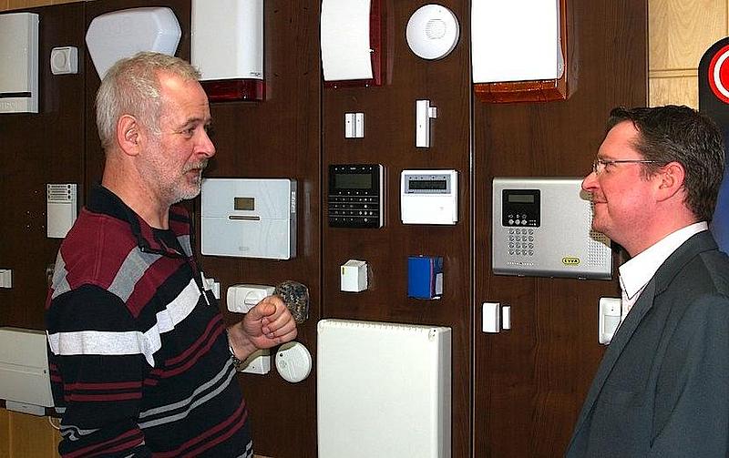 Bernd Liedl von Fa. Lissy Sicherheitssysteme vor einer Wand mit Alarmanlagen 
