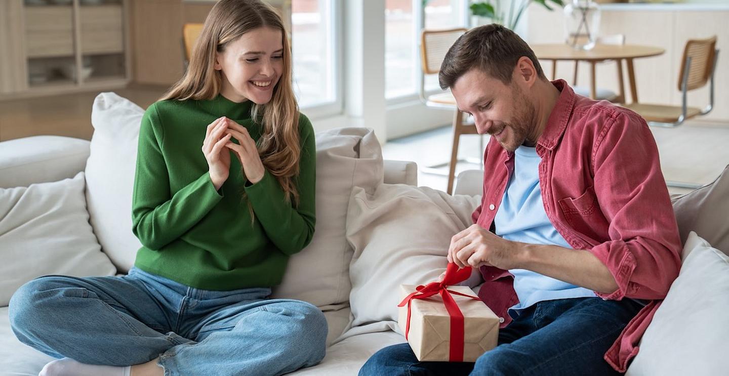 frau und mann mit Geschenk am Schoss sitzen auf couch 