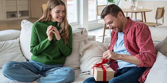 frau und mann mit Geschenk am Schoss sitzen auf couch 