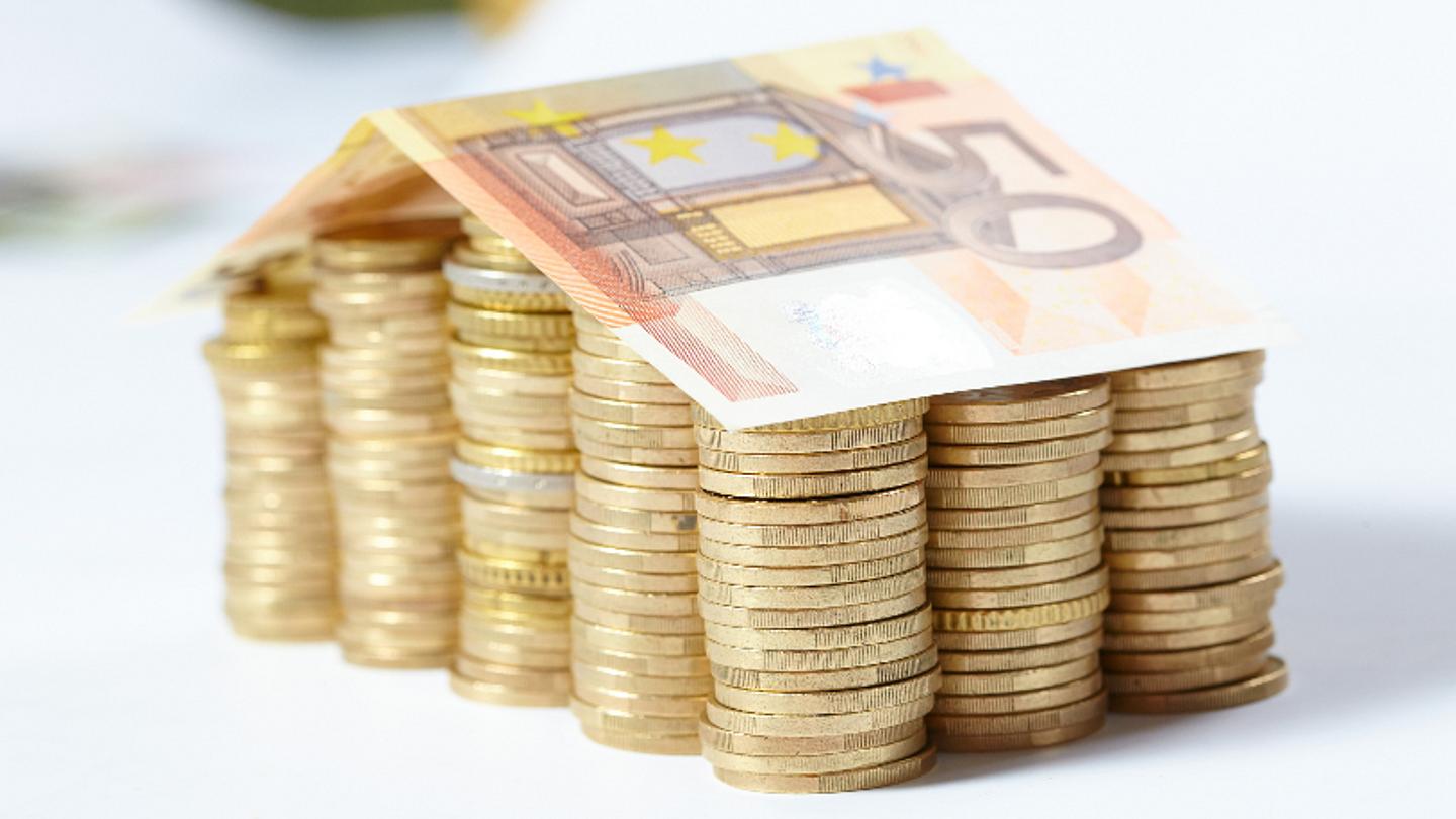 kleines Haus das aus Geld gebaut ist, gestapelte Münzen und ein 50-Euro-Dach