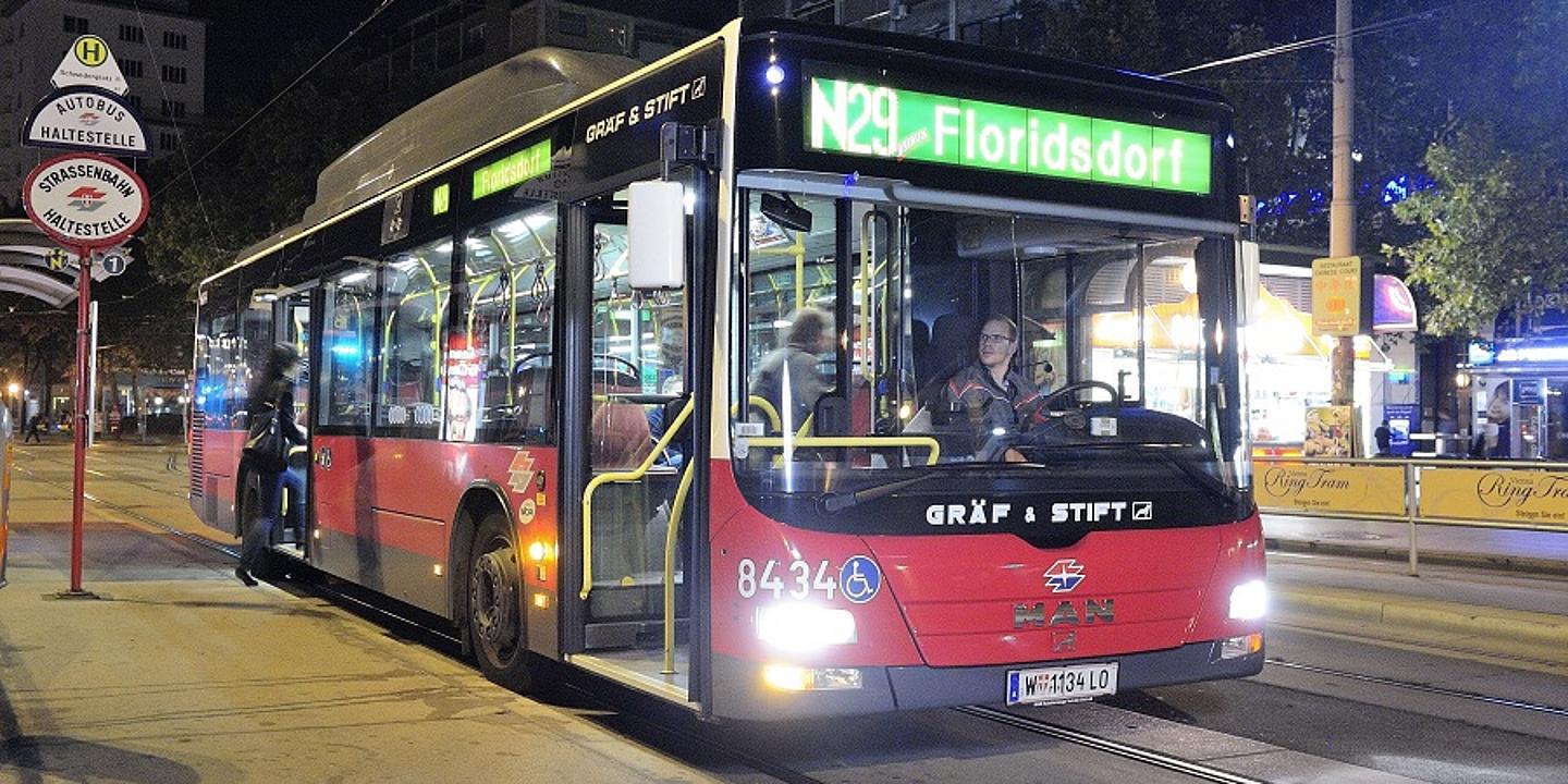 Bild von der Nightline N29 in Richtung Floridsdorf bei der Station Schwedenplatz. Zwei Personen steigen gerade zu. Im Hintergrund leuchten die Imbisbuden.