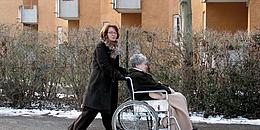Frau schiebt ältere Frau mit dem Rollstuhl.