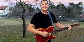 Viktor Gernot auf einem Feld mit Gitarre und Grinsen im Gesicht