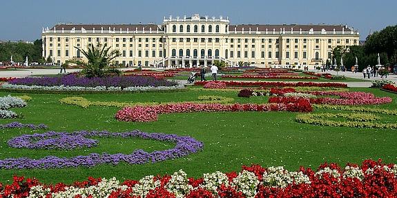 Bild von Schloss Schönbrunn - im Vordergrund der Garten mit roten, weißen, violetten, gelben und pinken Blumen.