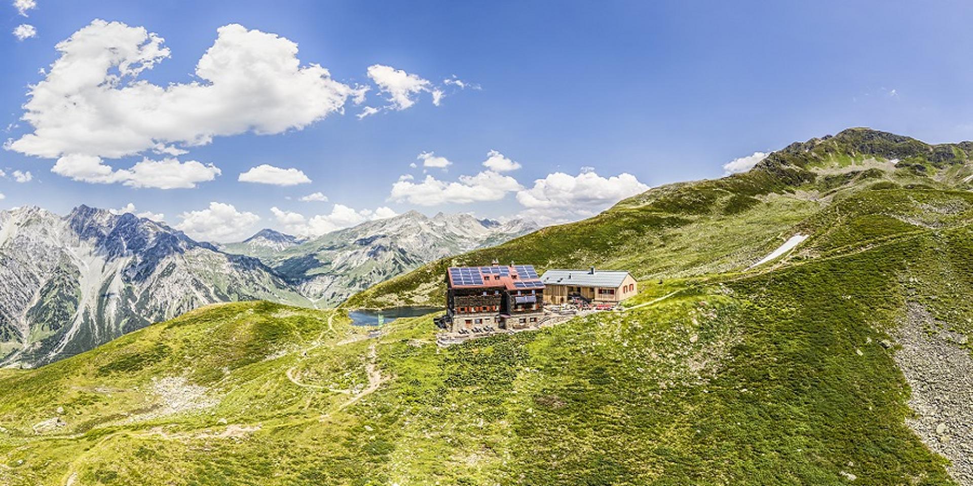 Kleine Almhütte auf grüner Wiese, im Hintergrund verschneiter Berg