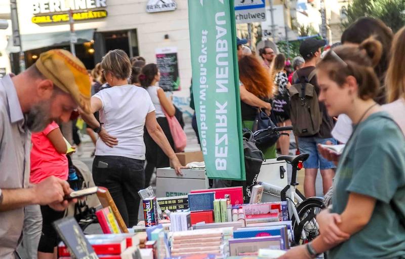 Besucher*innen stöbern in Büchern, lauschen Lesungen und genießen das Festival im Freien.