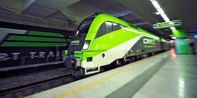 Dynamisches Bild eines einfahrenden City Airport Trains, kurz CAT, am menschenleeren Bahnsteig. Das grelle grün des Zuges steht in Kontrast mit der grauen Färbung der unterirdischen Station. Die Schrift der Anzeigetafel auf dem Bahnsteig ist verschwommen.