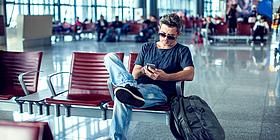Mann sitzt in Flughafen Wartehalle und schaut auf das Handy