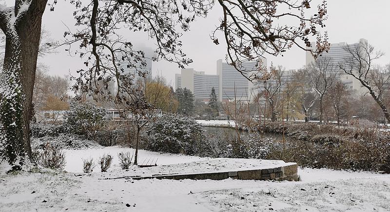 Das Vienna International Center ist im Hintergrund zu sehen, während im Vordergrund schneebedeckte Vegetation um einen Teich herum zu sehen ist