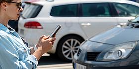 frau schaut auf Handy im Hintergrund autos