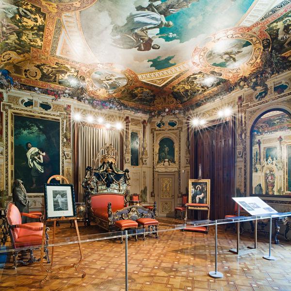 Ein prunkvolles Schlafzimmer mit vielen Wandgemälden, roter Sitzgarnitur und einem riesigen Deckengemälde.
