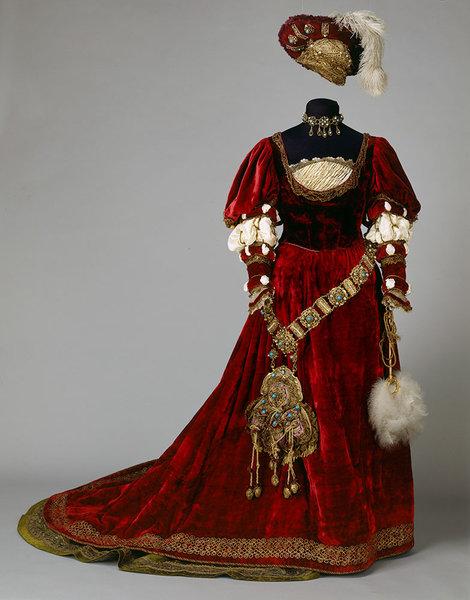 Rotes Samtkleid mit goldenenm Ziergürtel,weißen Puffärmeln und einem roten Samthut mit weißer Feder.
