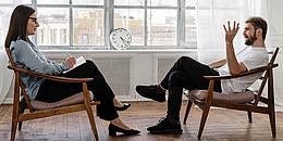 Das Bild zeigt zwei sprechende Personen, die sich in Sesseln gegenübersitzen.