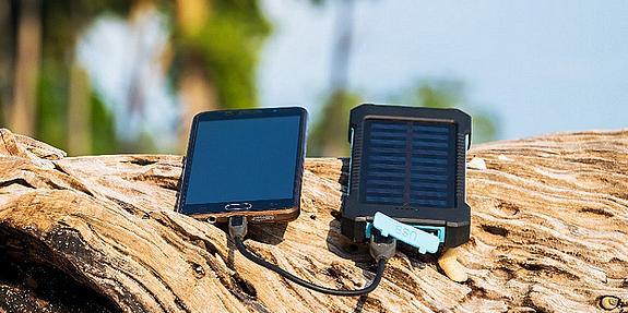 Solar Powerbank an der ein Handy angeschlossen ist liegt auf Baumstamm