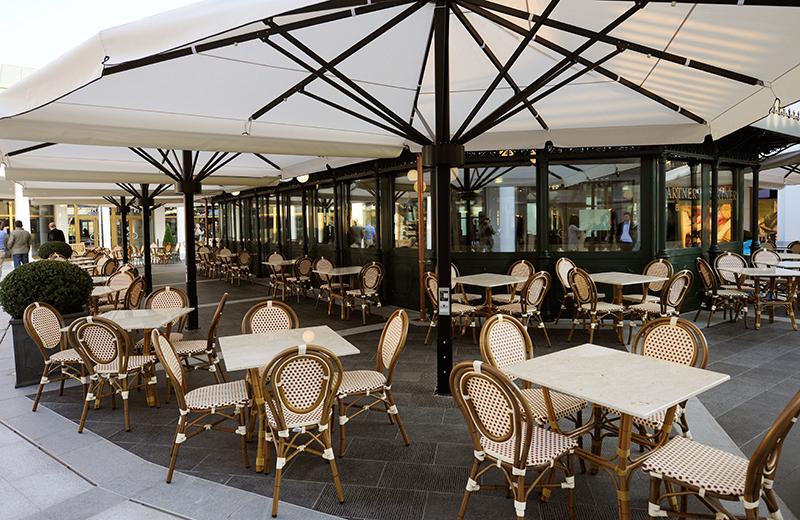 Tische und Sessel unter Schirmen vor einem Café im Designer Outlet Parndorf
