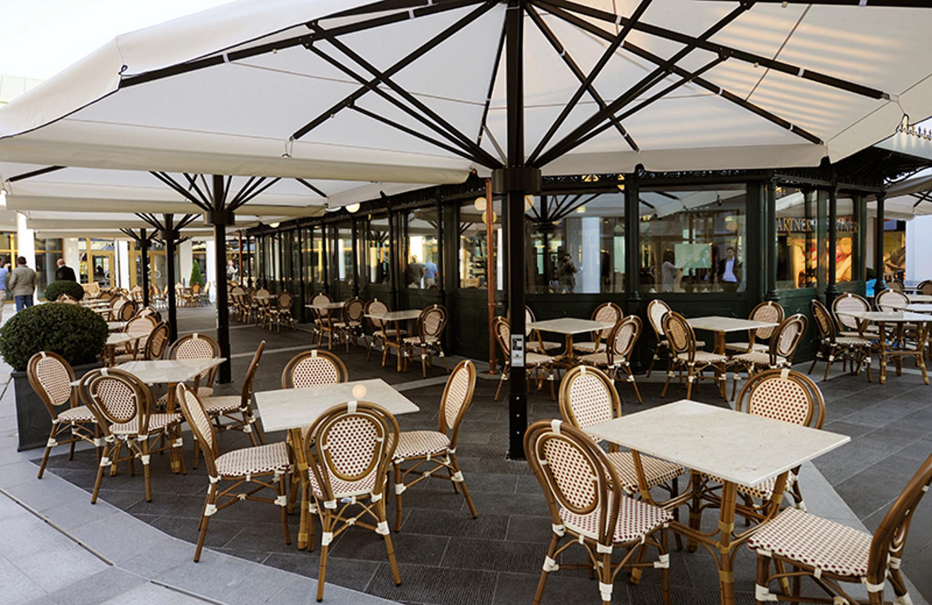 Tische und Sessel unter Schirmen vor einem Café im Designer Outlet Parndorf