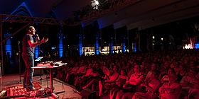 Wiener Kabarettfestival: Pro Abend zwei Kabarett-Programme Kabarettist Gernot Krulis vor Publikum auf der Bühne im Rotlicht