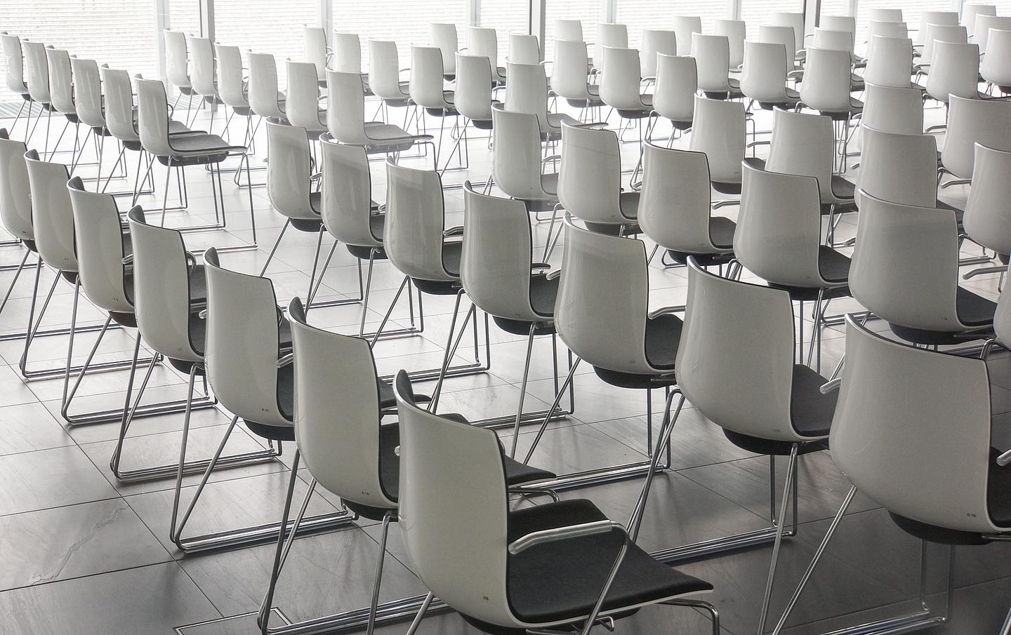 Hellgraue Stühle in Reihen in einem Seminarraum 