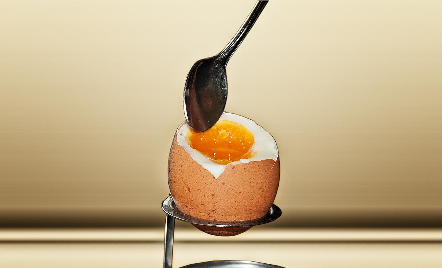 Aufgeschlagenes Frühstücksei, in das ein Löffel getaucht wird 