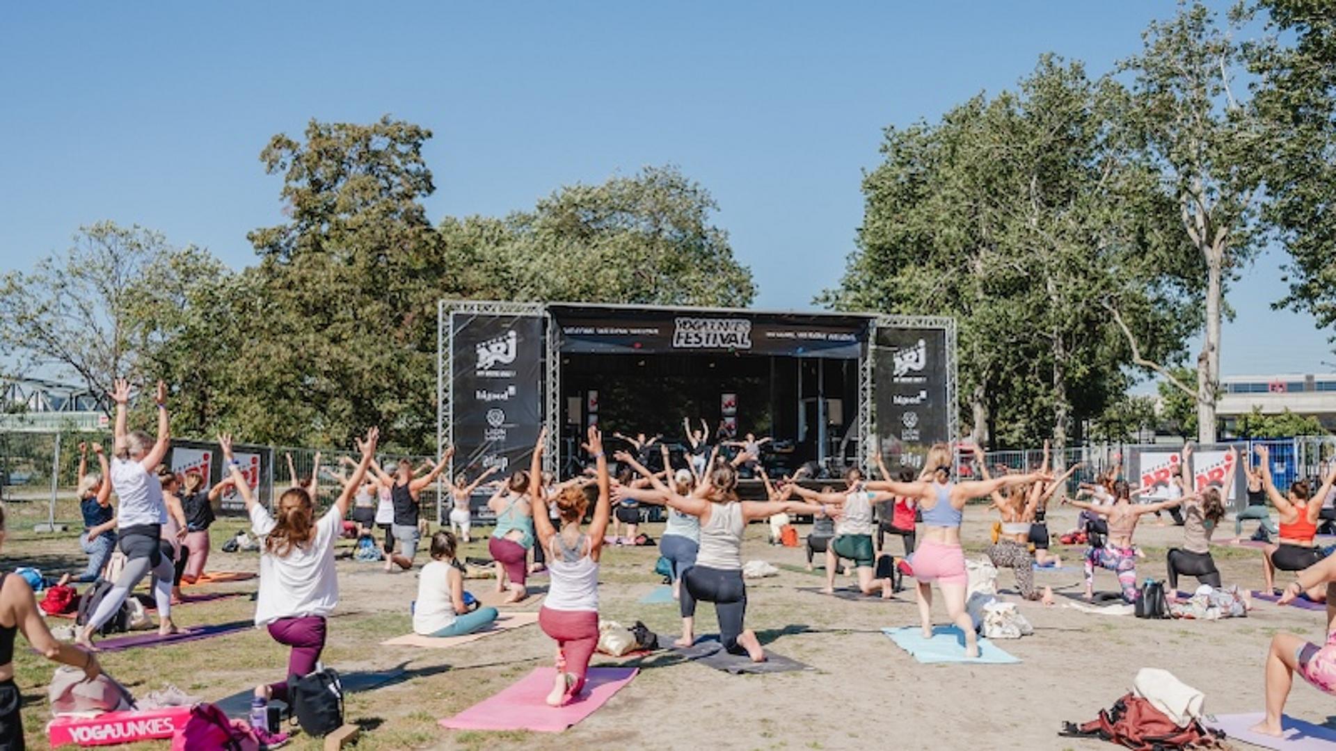 Eine Menschengruppe, die gemeinsam im Freien vor einer Bühne Yoga macht. 