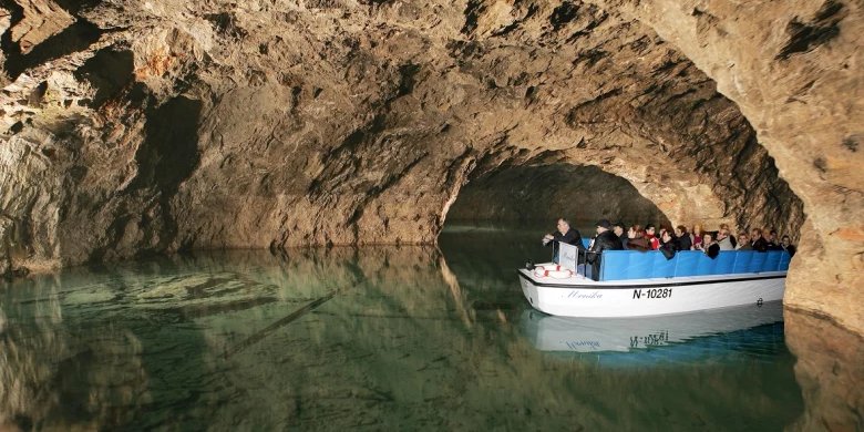 Kleine Besuchergruppe in einem Boot auf einem stillen, grünlich leuchtenden unterirdischen See, umgeben von dunklen Felswänden der Seegrotte Hinterbrühl