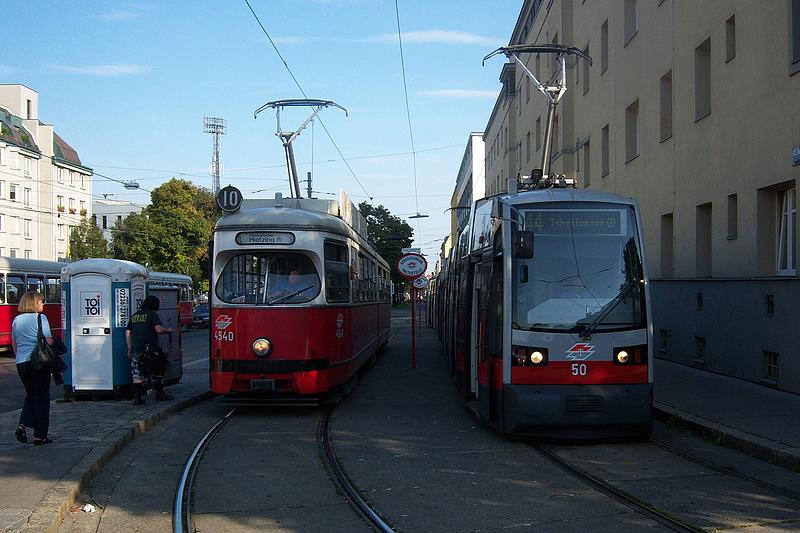 Bild von neuer Straßenbahngarnitur, die neben einer alten Straßenbahngarnitur vorbeifährt.