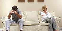 Mann und Frau an je einem Ende einer weißen Couch und voneinander abgewandt 