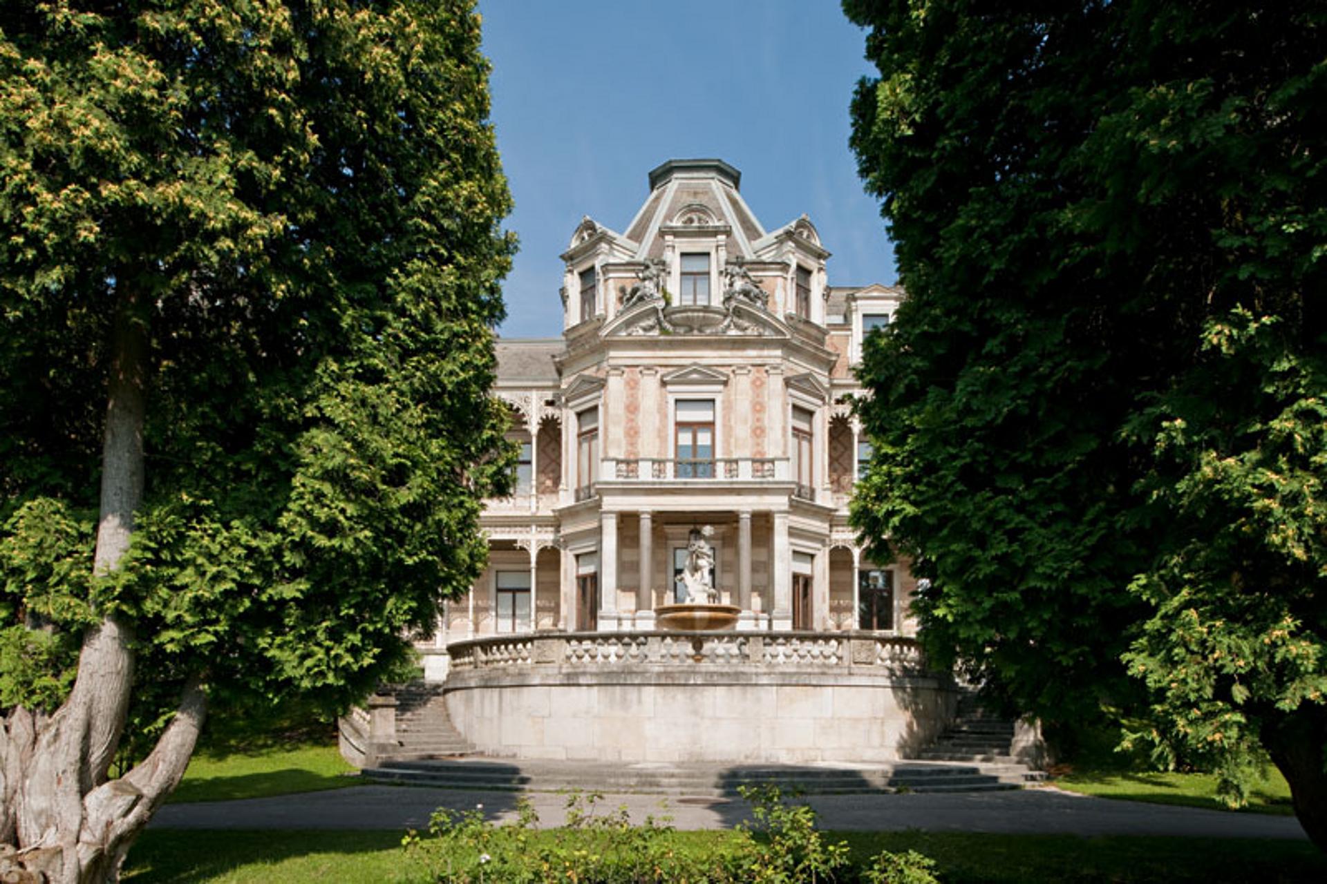 Eine prächtige rosafarbene Villa, davor links und rechts zwei Bäume.