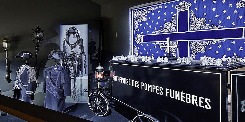 Ein alter Leichenwagen, zwei blaue Uniformen, ein Kreuz