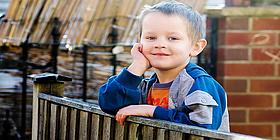Kinderprogramm Mai Kleine Junge der auf Balkongeländer lehnt und in die Kamera grinst