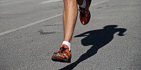 Beine eines Joggers und dessen Schatten auf dem Asphalt